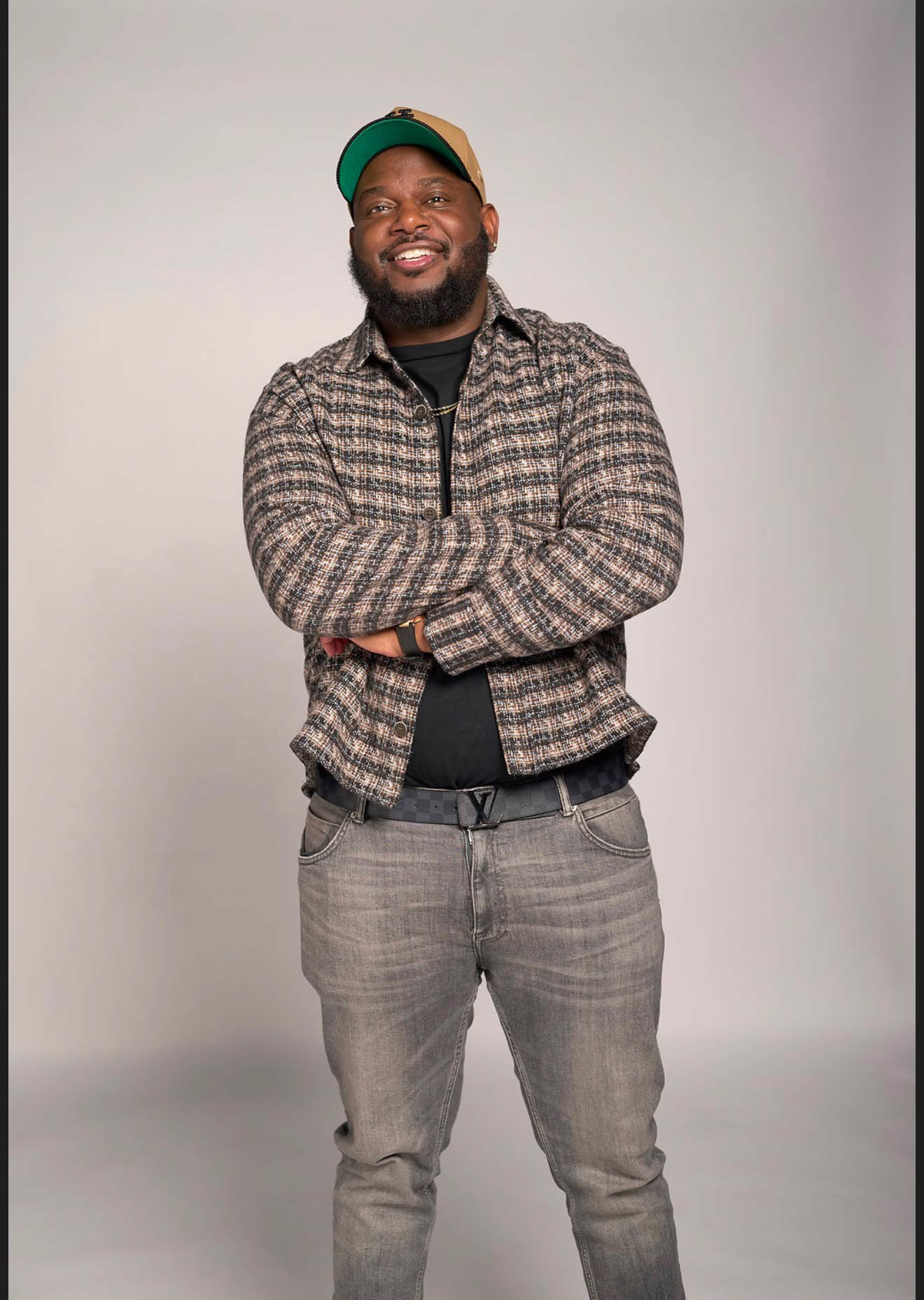 BTIDY standing with his arms crossed in a green‑and‑tan cap.